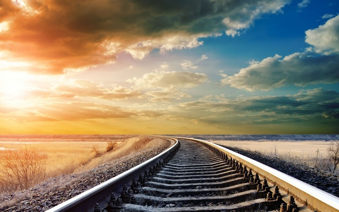 Railway tracks curving through a landscape at sunset