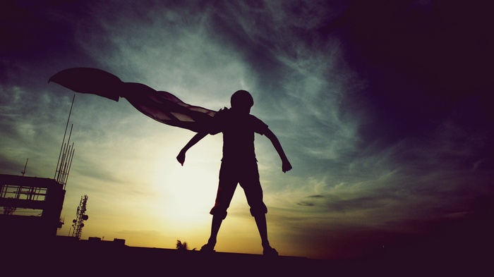 Silhouette of a child with a cape at sunset