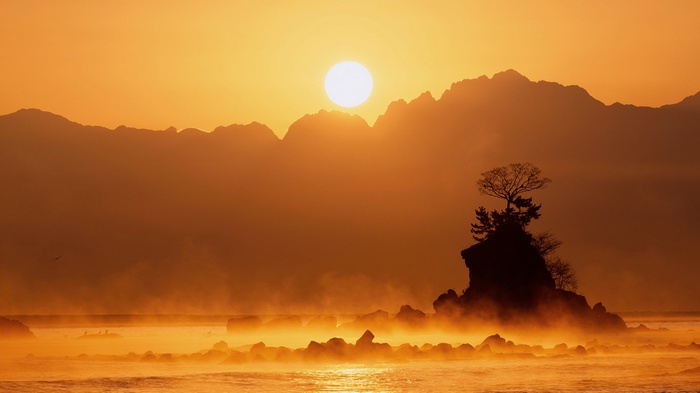 Sunrise over misty mountains and a rocky island with a tree