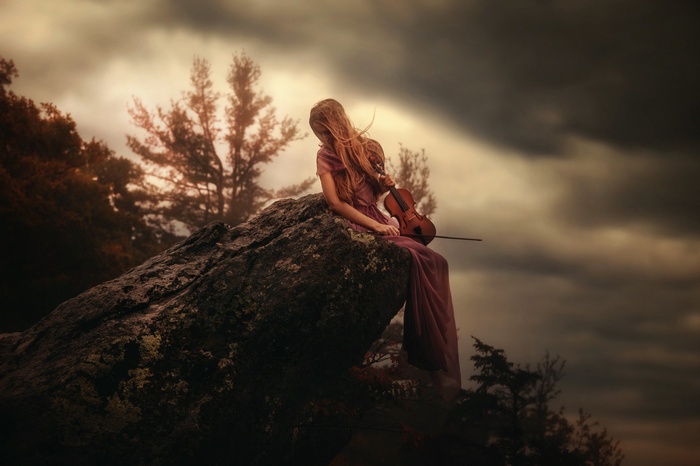 Woman with violin sitting on a rock