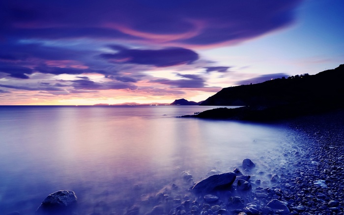 Purple sunset over a rocky coast and calm sea