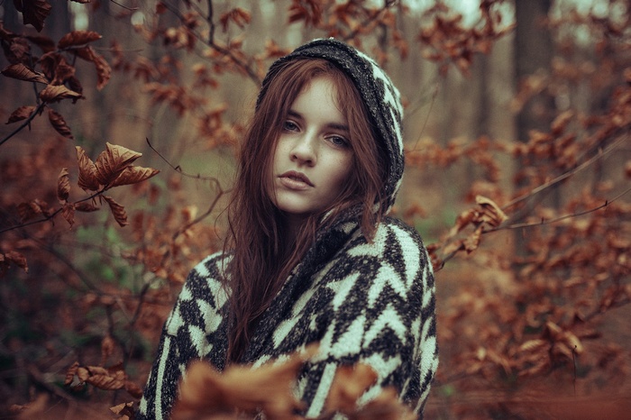 Redhead woman with freckles wearing a hooded sweater in a forest