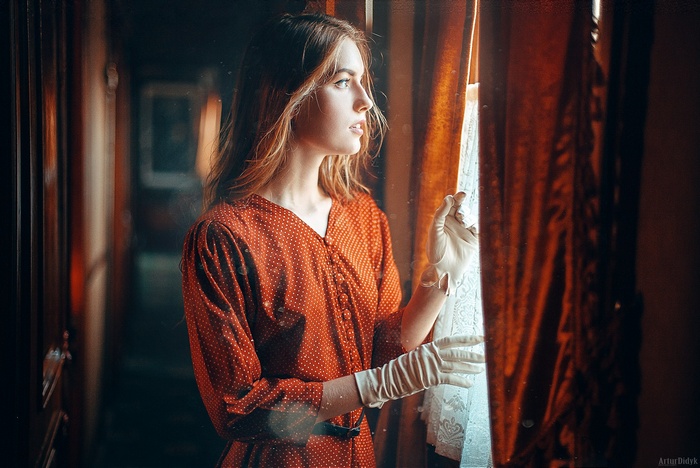Woman in a red polka dot dress looking out a window