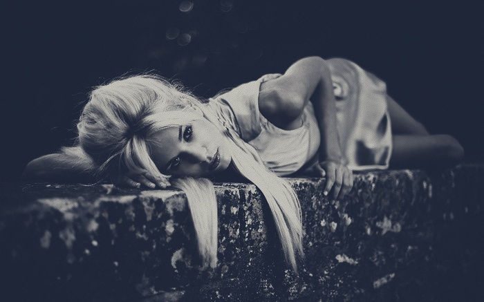 Blonde woman lying on a stone ledge