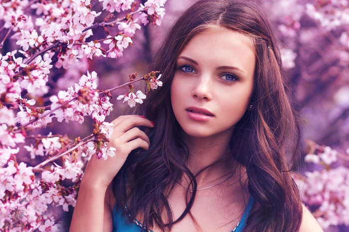 Woman with brunette hair and blue eyes among cherry blossoms