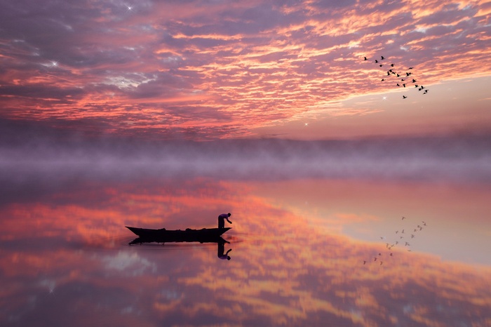 Fisherman in a boat on a lake at sunset with birds flying