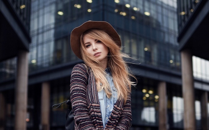 Woman with blonde hair and hat in front of modern building