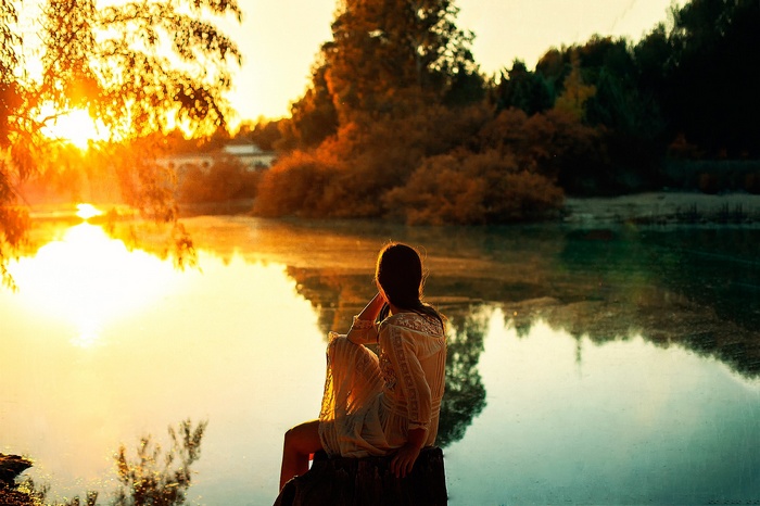 Woman sitting by a lake at sunset
