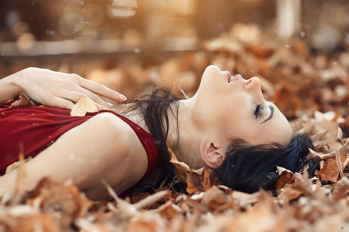 Woman in red dress lying on autumn leaves