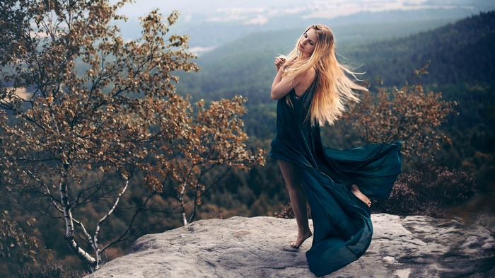 Woman in a flowing dress on a rocky cliff overlooking a forest