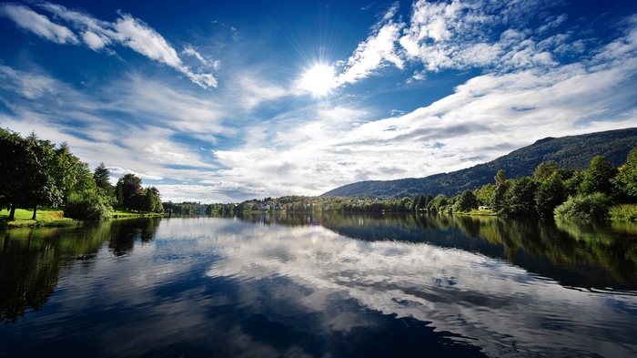 Lake with mountains and trees under a sunny sky
