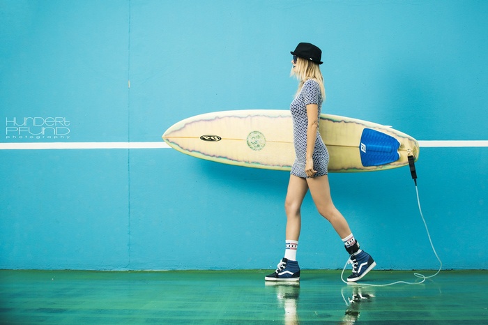 Woman with surfboard and Hundertpfund photography logo