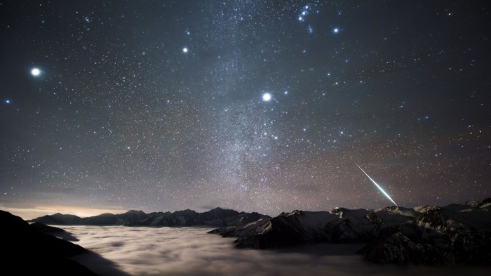 Meteor shower over snowy mountains and clouds under the galaxy