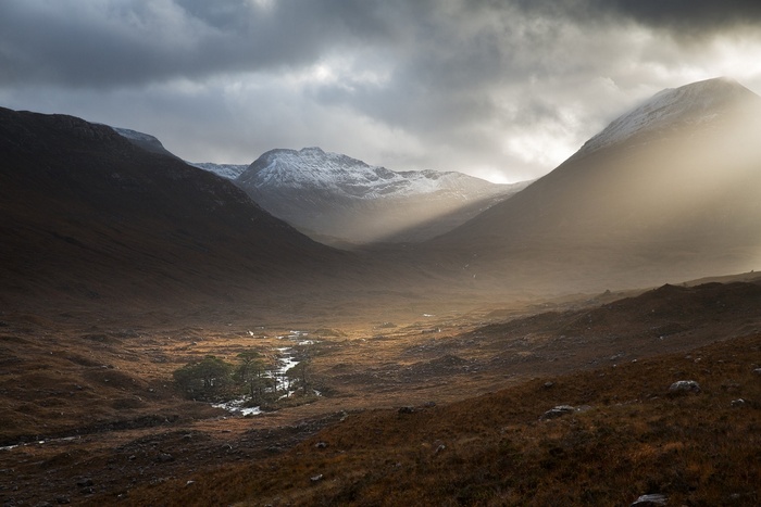Sunlight beams through a mountain valley with a river