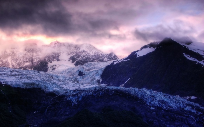 Dark mountains with glaciers and clouds at sunset