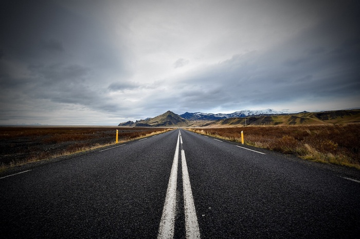 Road leading to mountains under cloudy sky