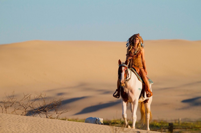 Woman in Native American Headdress Riding Horse in Desert