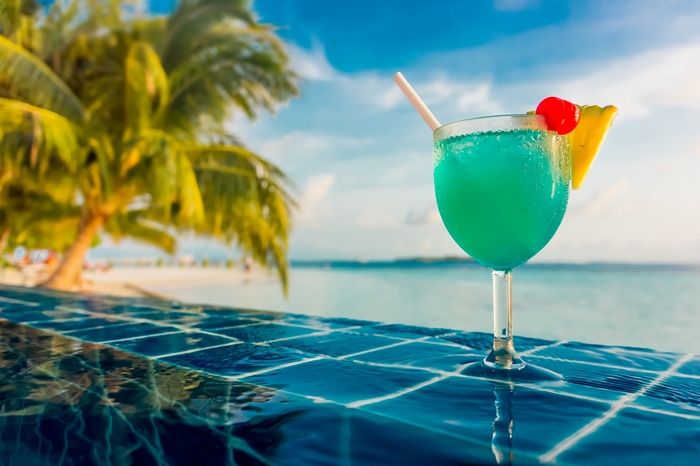 Blue cocktail by the infinity pool with palm trees and ocean