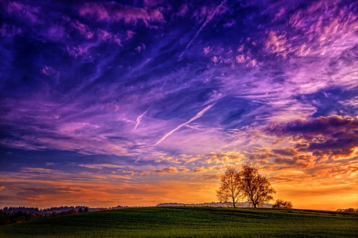 Dramatic sunset sky over a green hill with trees