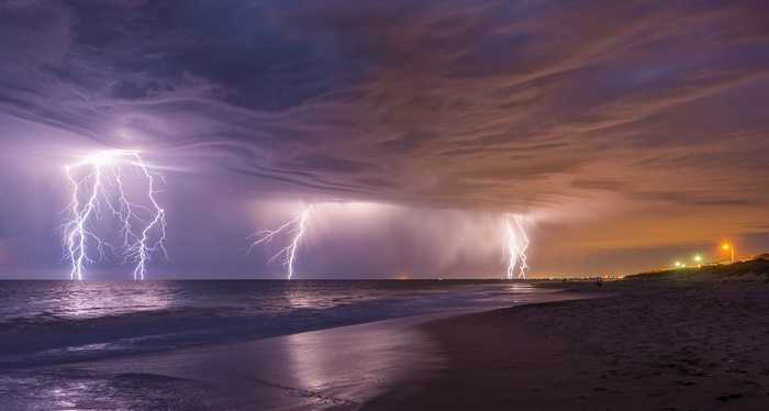 Lightning strikes over the ocean and beach at night