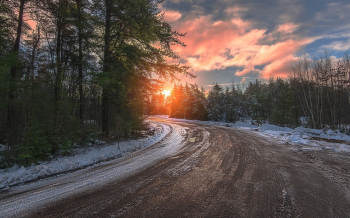 Road through a forest at sunset with snow