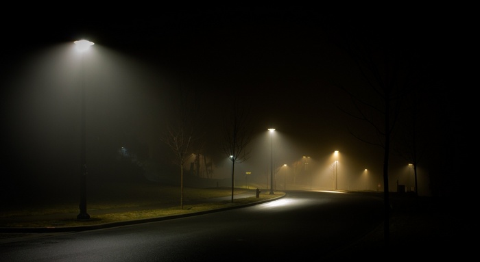 Street lights illuminate a foggy road at night