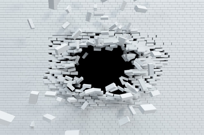 White brick wall breaking apart with debris flying