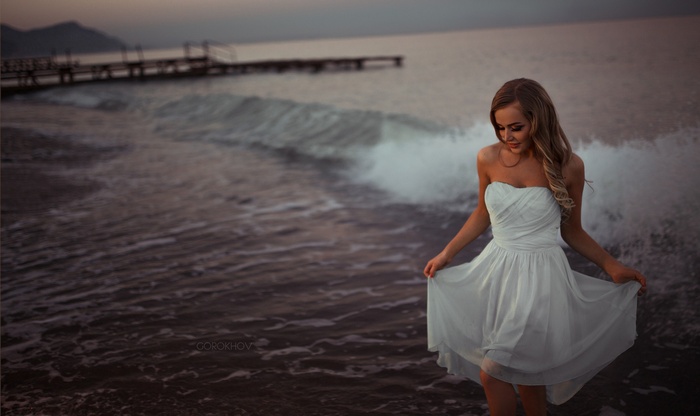 Woman in white dress on beach with pier at sunset