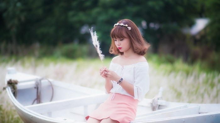Woman in white top and pink skirt sitting in a boat