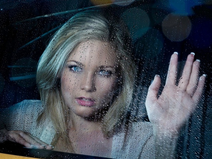 Woman with blonde hair and blue eyes looking through a rainy window