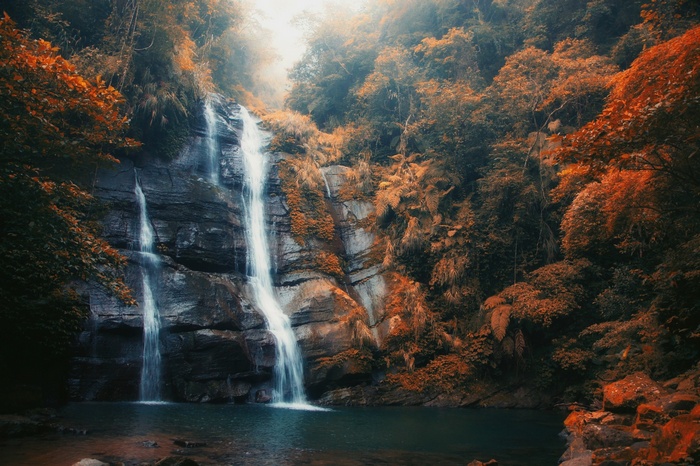 Waterfall cascading through a forest with autumn leaves