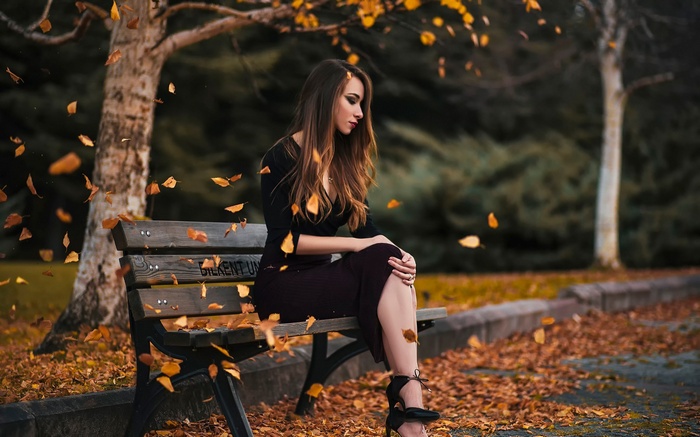 Woman in black dress sitting on a bench in autumn