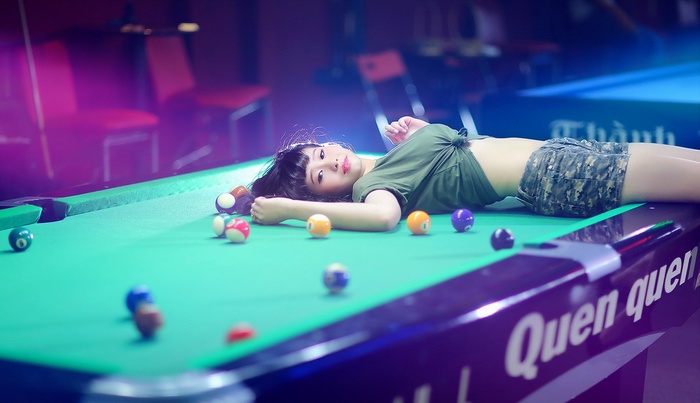 Asian woman lying on a pool table with billiard balls
