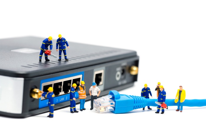 Miniature workers repair a router with a blue ethernet cable