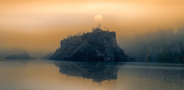 Misty lake with rocky island and sun reflection