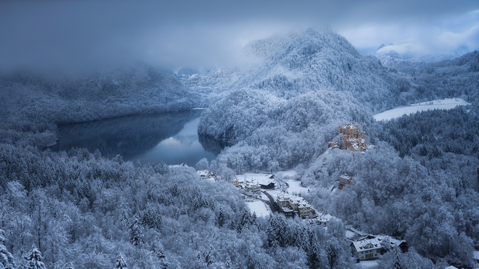 Winter landscape with a castle overlooking a snowy forest and lake