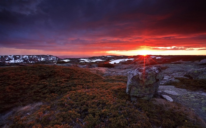 Dramatic sunset over a rocky, barren landscape with snow patches