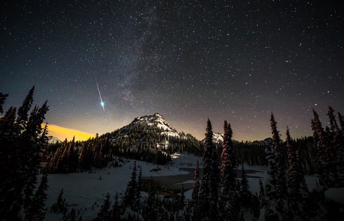 Meteor shower over snowy mountains and pine trees