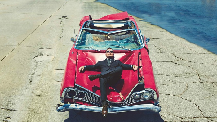 Bryan Cranston in a suit on a damaged car