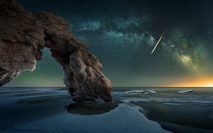Milky Way over icy rock arch and frozen sea