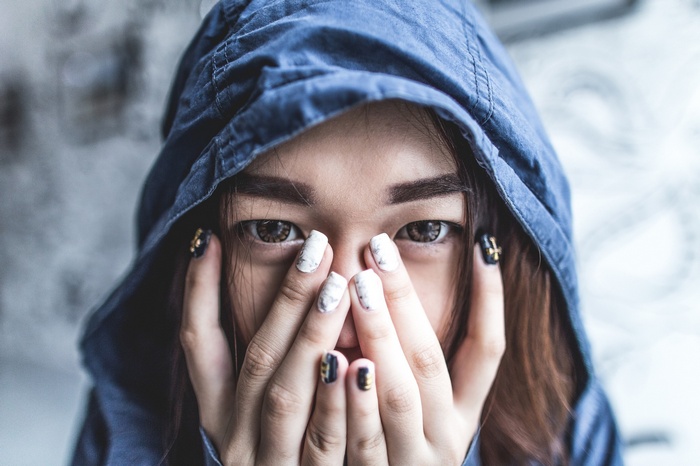 Woman hiding face with hands under blue hood