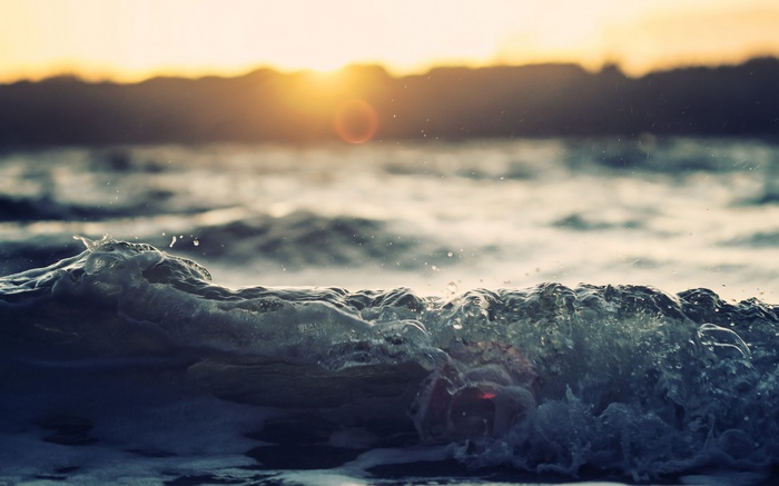 Ocean wave at sunset with sun flare