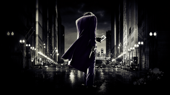 The Joker holding a playing card in a city at night