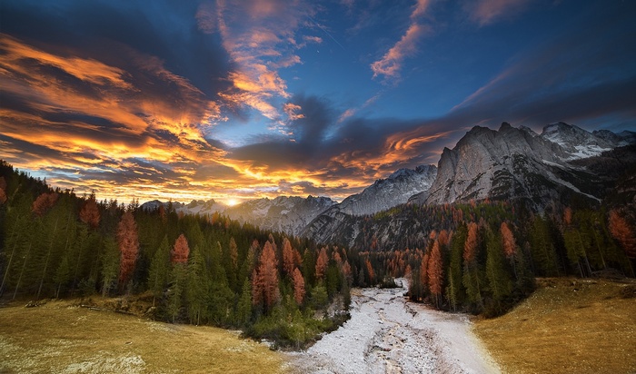 Sunset over a mountain range with a forest and dry riverbed