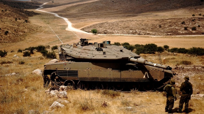 Merkava Mark IV tank with soldiers in a dry, hilly landscape