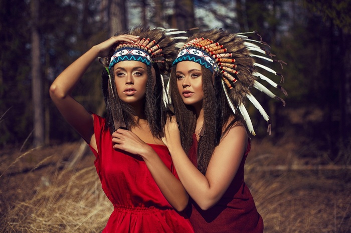 Two women wearing Native American headdresses in a forest