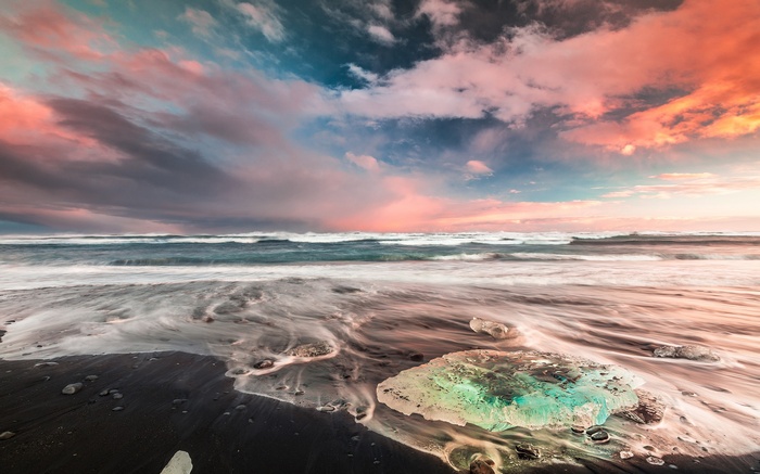Ice chunks on black sand beach with colorful sunset sky