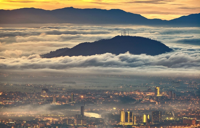 Cityscape shrouded in mist below mountains at sunrise
