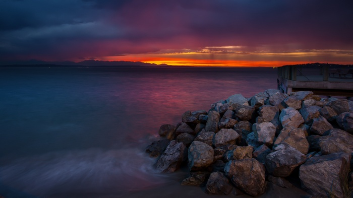 Sunset over the sea with rocks and a pier