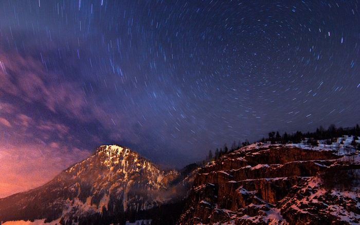 Star trails over snow-covered mountains at night